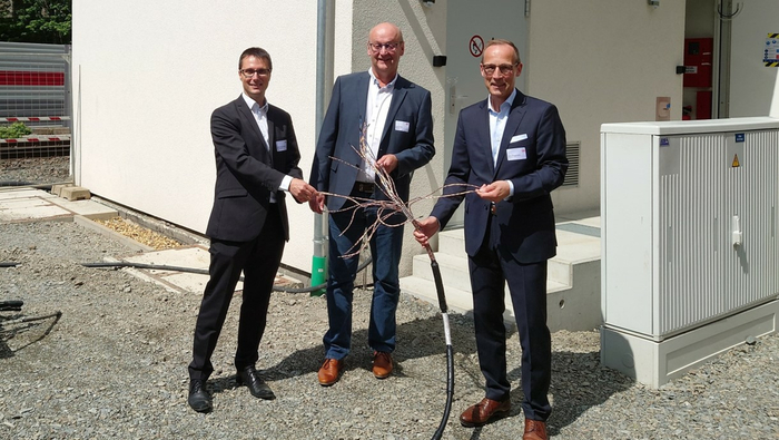 Drei Männer stehen vor einem Gebäude und halten ein Kabel in den Händen.