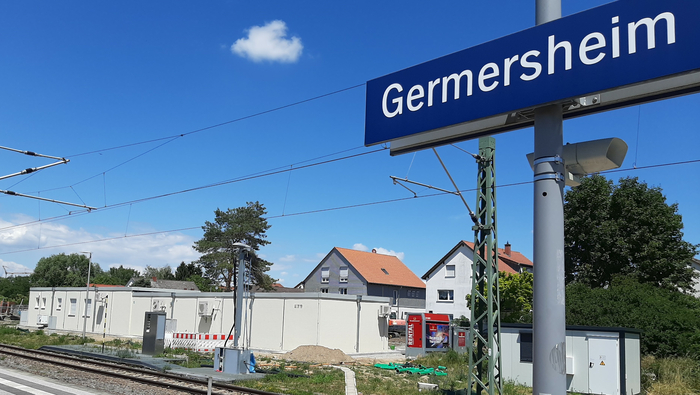Sicht vom Bahnsteig auf ein flaches Gebäude im Hintergrund. Das blaue Schild auf dem Bahnsteigt schreibt "Germersheim".